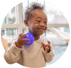 Young child with Downs Syndrome smiling while playing with a ball.