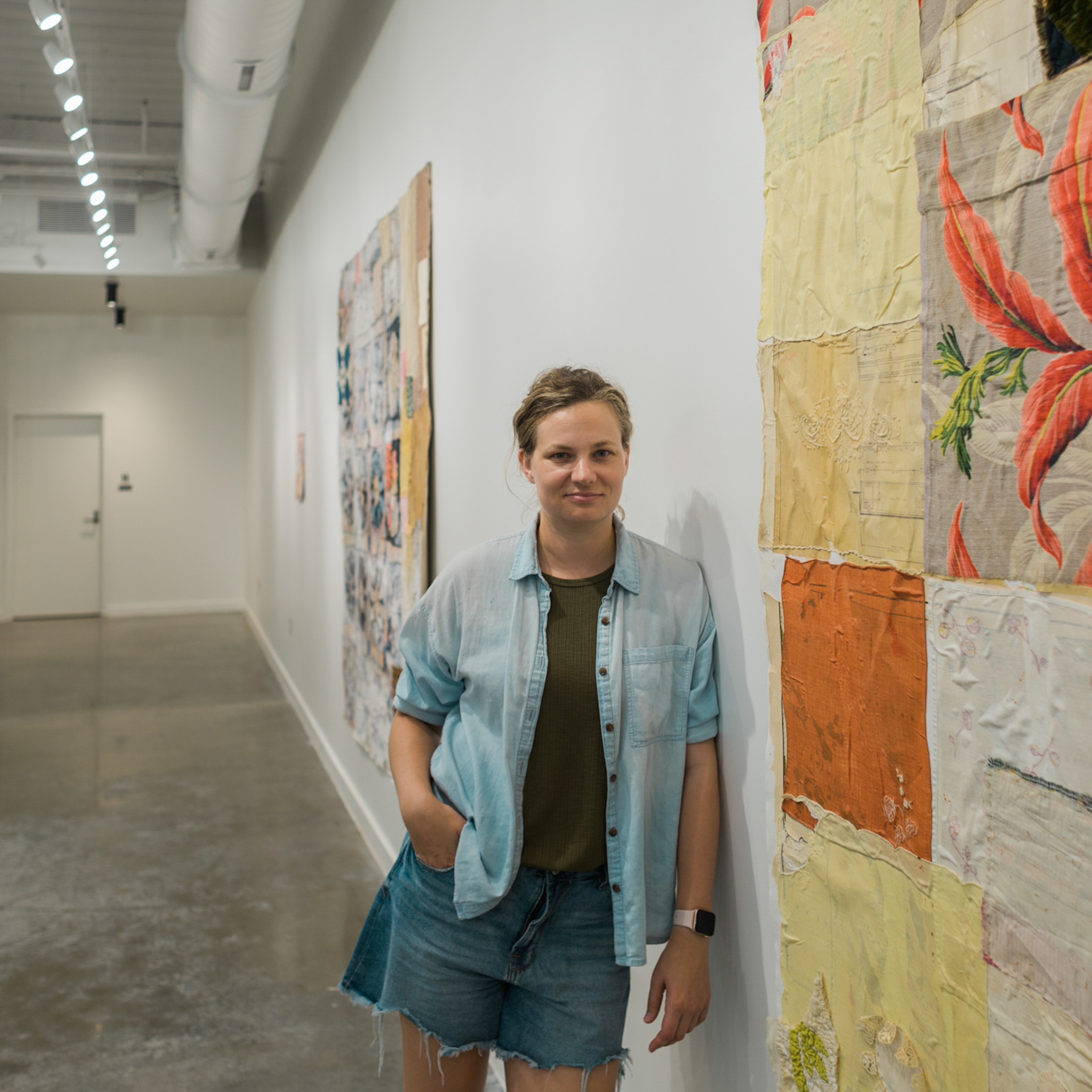 Woman leaning on wall next to artwork.
