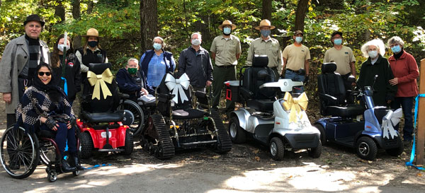 Group photo of people standing behind motorized wheel chairs.