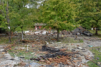 Scene of an exploded structure in rural area with burned building materials scattered