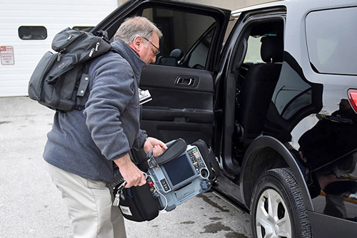 Community paramedic carries portable cardiac monitor to a van
