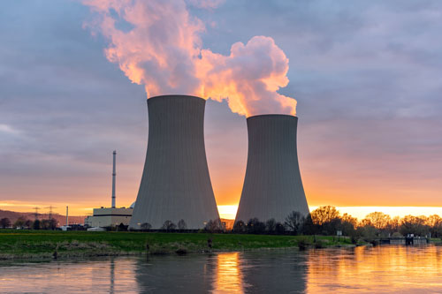 Nuclear power plant cooling towers by water at sunset