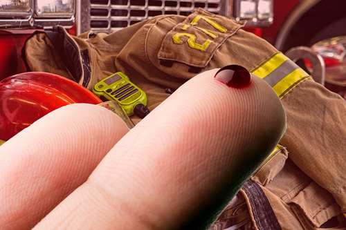 Drop of blood on finger with fire gear in background