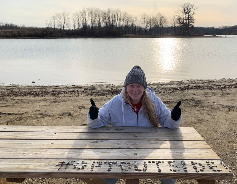 Person at picnic table with rocks spelling optoutside