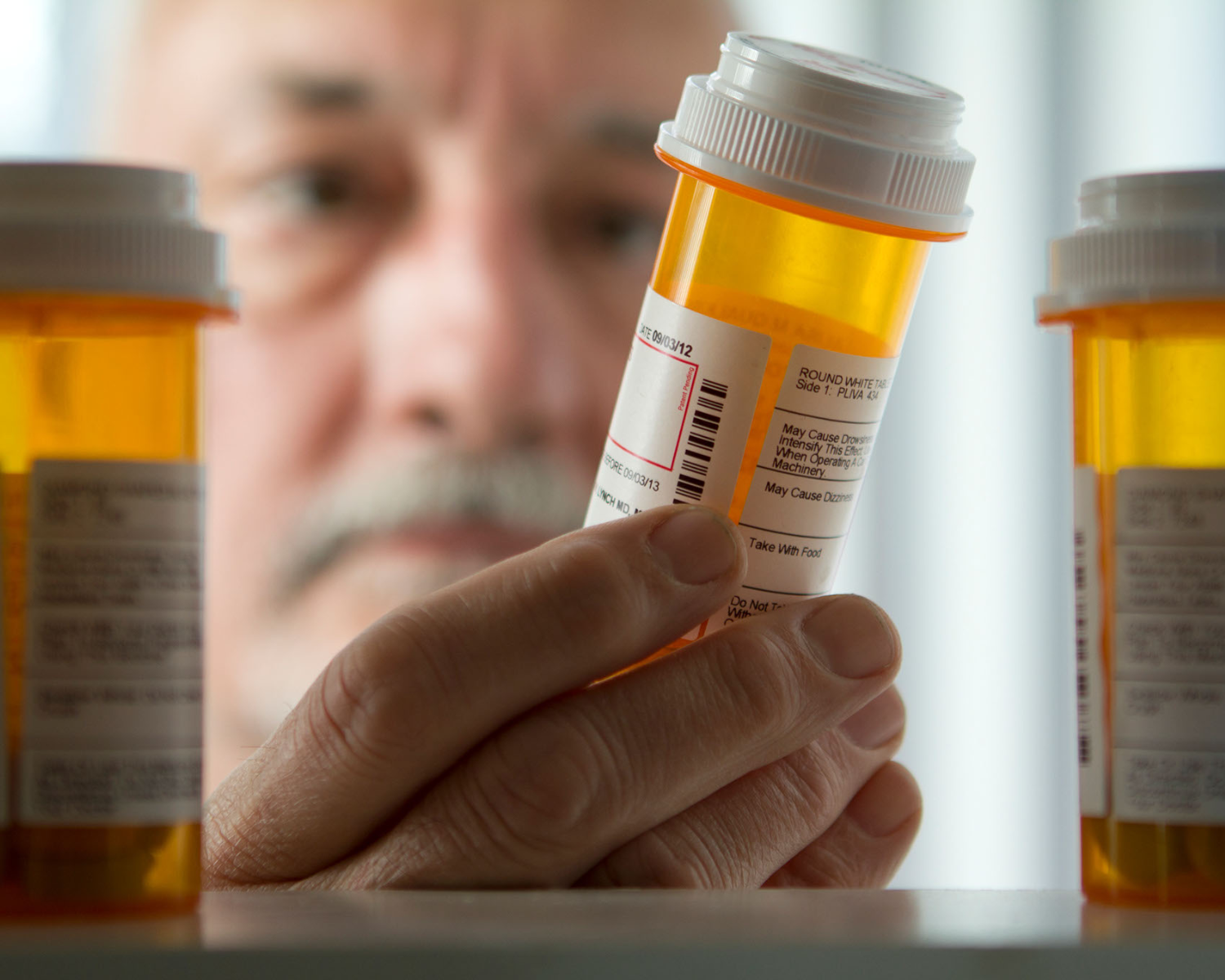 old white man looking at prescription pill bottle