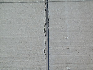 Close-up photo of a transverse joint with low-severity joint seal damage.  The silicone sealant in the photo           is in good condition, but it is noticeably debonded from one side of the joint.