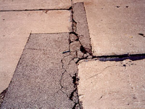 Close-up photo of an irregularly shaped asphalt patch within a PCC slab. The patch           contains considerable visible distress that includes spalling, cracking, and a noticeable loss of material.