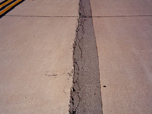 Overview photo of a longitudinal joint with a long narrow asphalt patch along the joint.           The patch is showing visible signs of distress, with spalling and secondary cracking along one side of the patch.